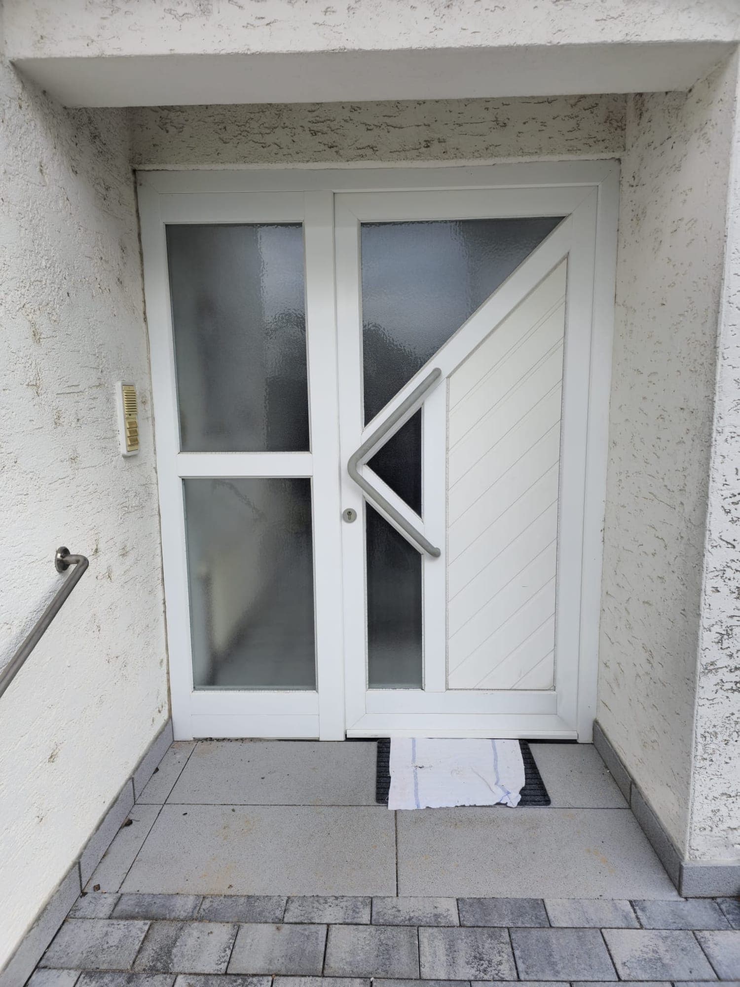 Eingebaute Haustür in Weiß mit diagonaler Edelstahl-Griffleiste und Seitenteil