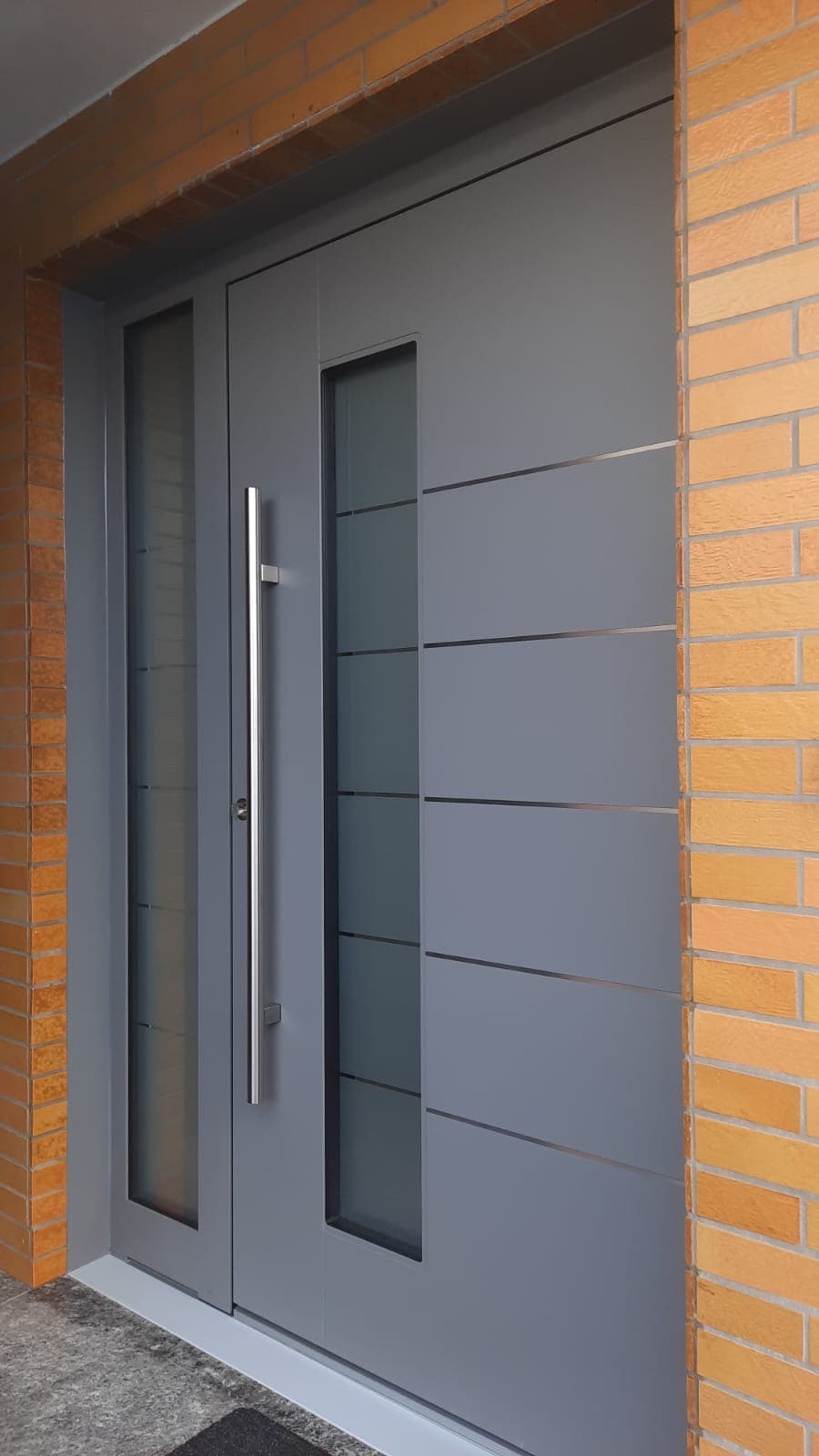 Eingebaute Haustür in Grau mit Edelstahl-Applikationen und Seitenteil an Klinkerfassade, Referenz aus dem Rhein-Main-Gebiet